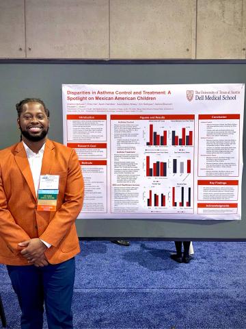 A man in an orange blazer stands in front of a poster display at a conference.