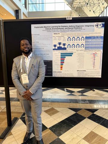 A man wears a grey suit and stands in front of a poster display.