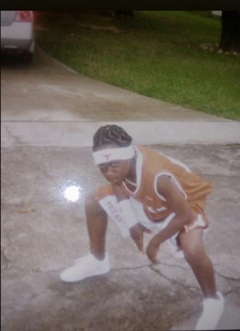 A kid wears UT sportswear and kneels in a driveway.