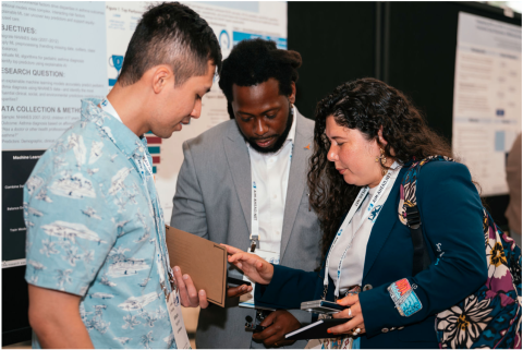 Three people in businesswear stand in front of a poster display.