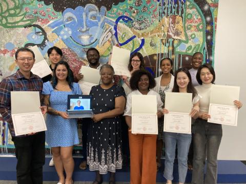 A group of people stand holding certificates in front of a mural.