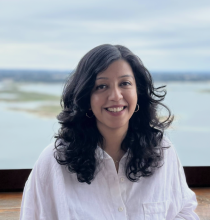 A person wears a white shirt and stands in front of a lake.