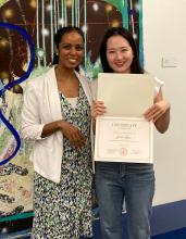 Yelim Hong poses with her teaching academy certificate next to Lydia Contreras as they both stand in front of a mural.