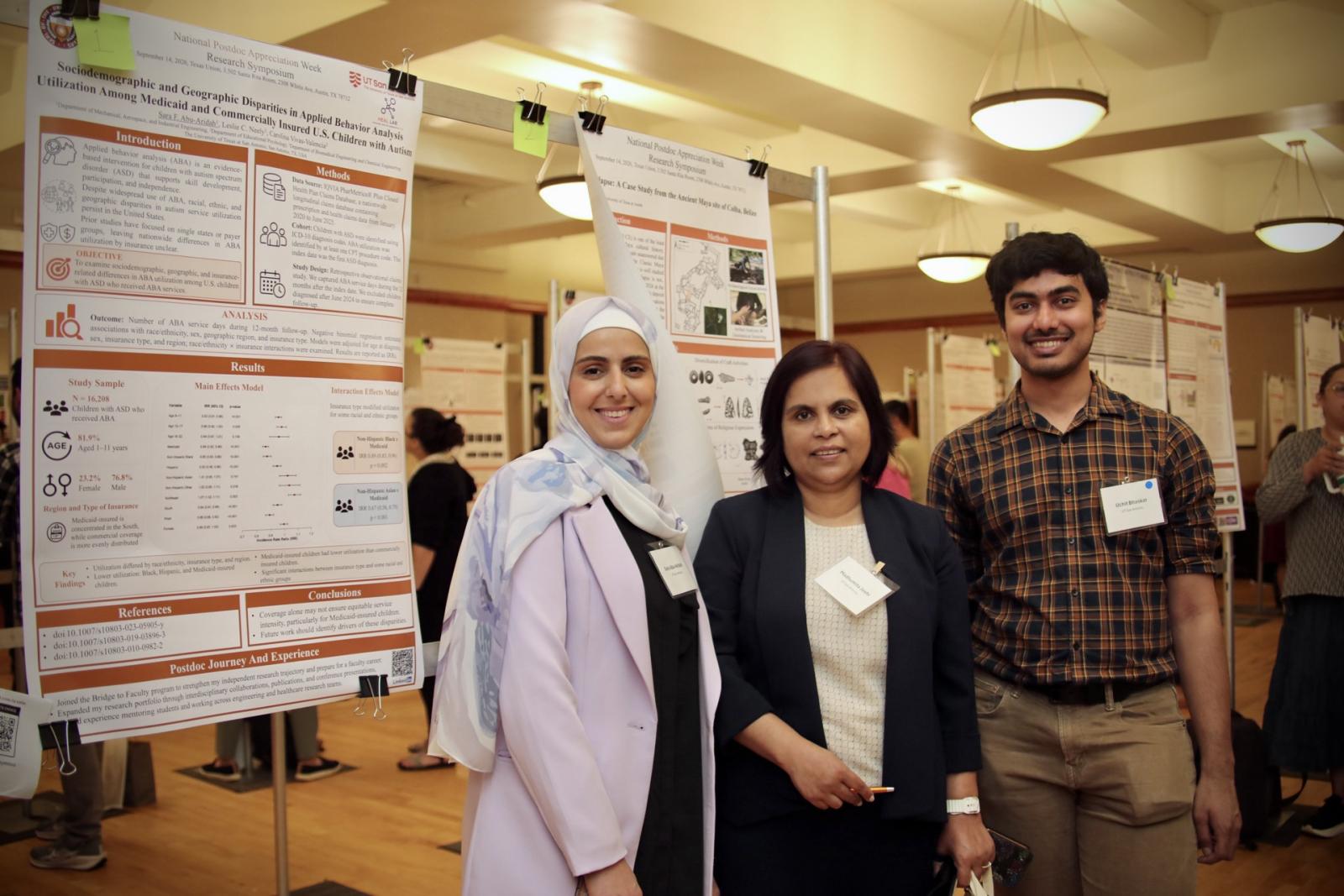 Three postdocs stand in front of posters during poster session