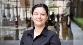 A woman wears a black blouse and stands outdoors.