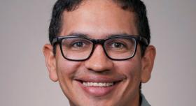 A person with glasses poses for a headshot in front of a grey background