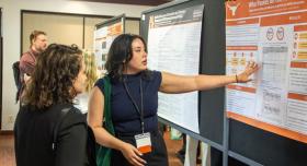 Two researchers stand in front of a poster on display at a conference.