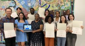 Fellows of the Postdoctoral Teaching Academy pose with their certificates in front of a mural.
