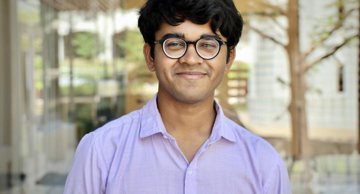 A man wears a lavender shirt and stands outdoors.