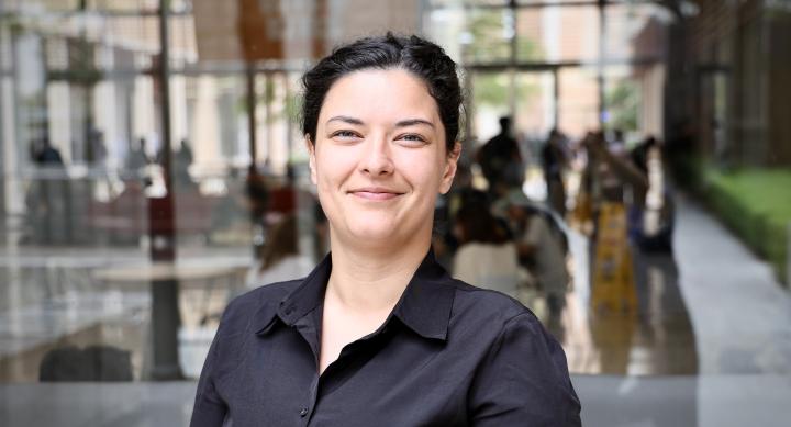 A woman wears a black blouse and stands outdoors.