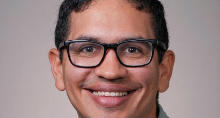 A person with glasses poses for a headshot in front of a grey background